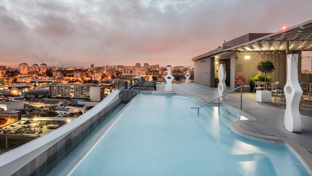 A rooftop infinity pool with a city view, outdoor seating, and a covered area with string lights. - Eurostars Universal Lisboa (Lisbon)