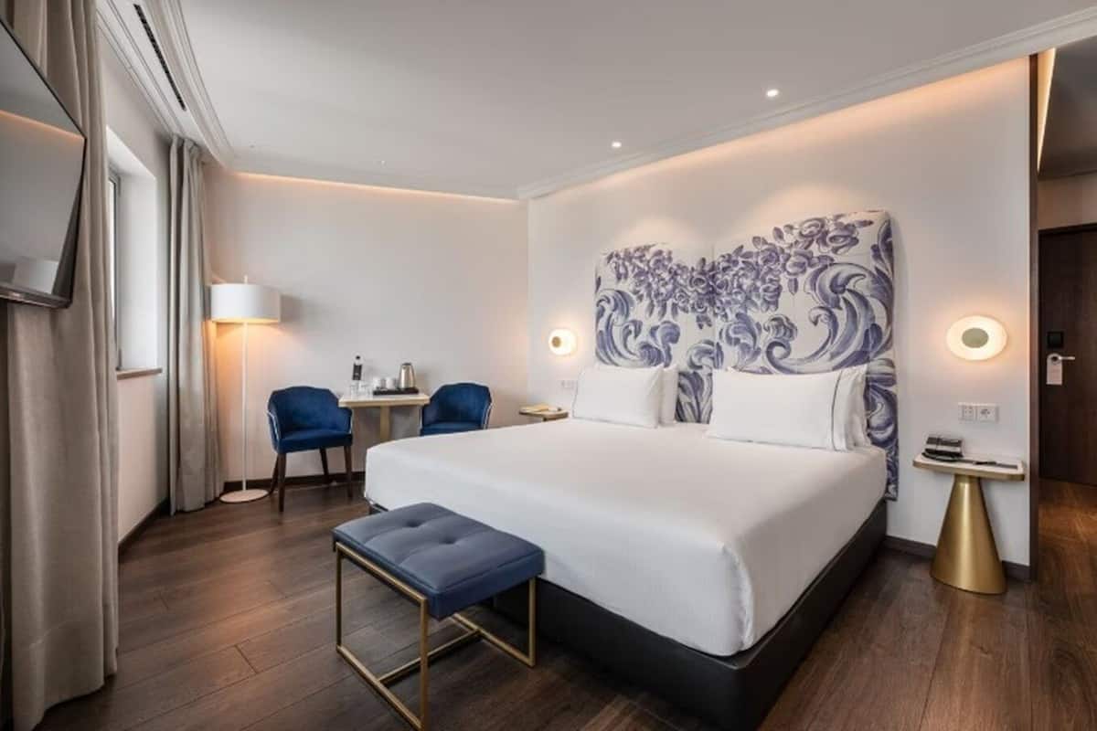 Ein Hotelzimmer mit einem großen Bett, einem Schreibtisch mit zwei Stühlen, einem kleinen Tisch und einem an der Wand montierten Fernseher.