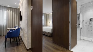 A hotel room with a wooden floor, a bed, a bathroom with a shower, and a seating area with a table and chairs.