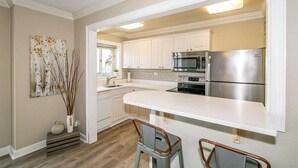 Una cocina con armarios blancos, electrodomésticos de acero inoxidable y encimera blanca.