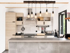 A modern kitchen with wooden cabinets, a central island, hanging pendant lights, and a window providing natural light.