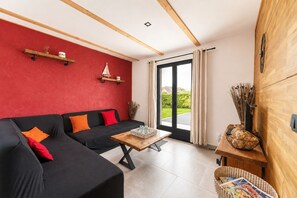 A modern living room with a black sofa, red cushions, a wooden coffee table, and a view through a glass door. - Elegant and cosy 3 star house, walking distance from the Teven beach (Île-Tudy)
