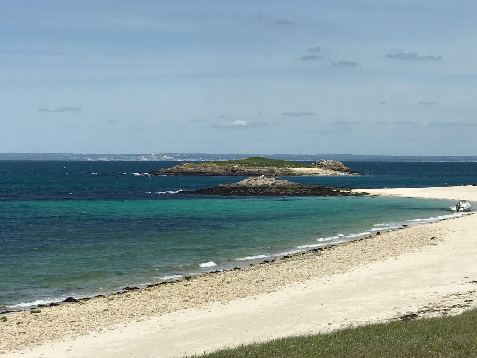 Une plage aux eaux turquoise et limpides, un rivage sablonneux et, au loin, des formations rocheuses.