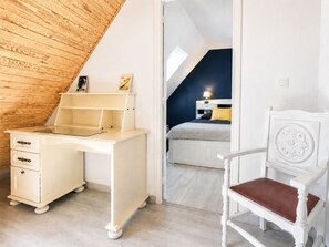 Een slaapkamer met schuine wand, een bureau, een stoel en een bed met nachtkastje.