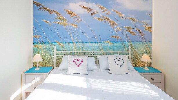 Een slaapkamer met een bed, wit beddengoed en een muurschildering met een strandthema.