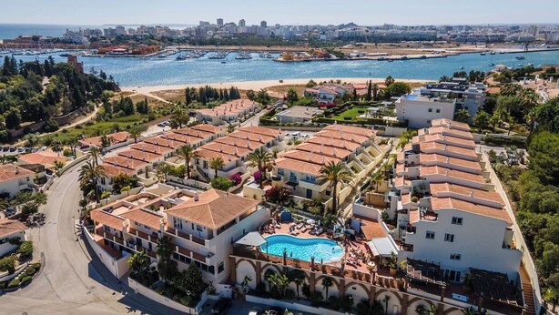 Ett bostadsområde vid kusten med radhus, en swimmingpool och en småbåtshamn i bakgrunden.
