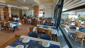 Un restaurante con varias mesas y sillas, una barra y grandes ventanales que ofrecen vistas al exterior.