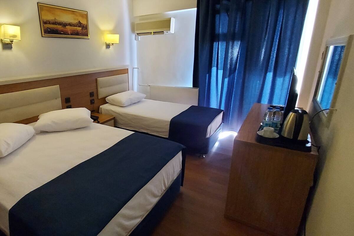 Ein Hotelzimmer mit zwei Betten, einem Holz-Kopfteil, einem Bild an der Wand und einem Fenster mit Vorhängen.