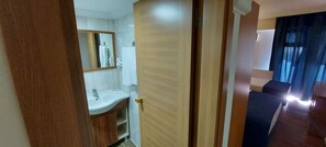 A hotel room with a wooden door, a white sink, a mirror, and a view of the hallway. - Blue Port Hotel (Burhaniye)