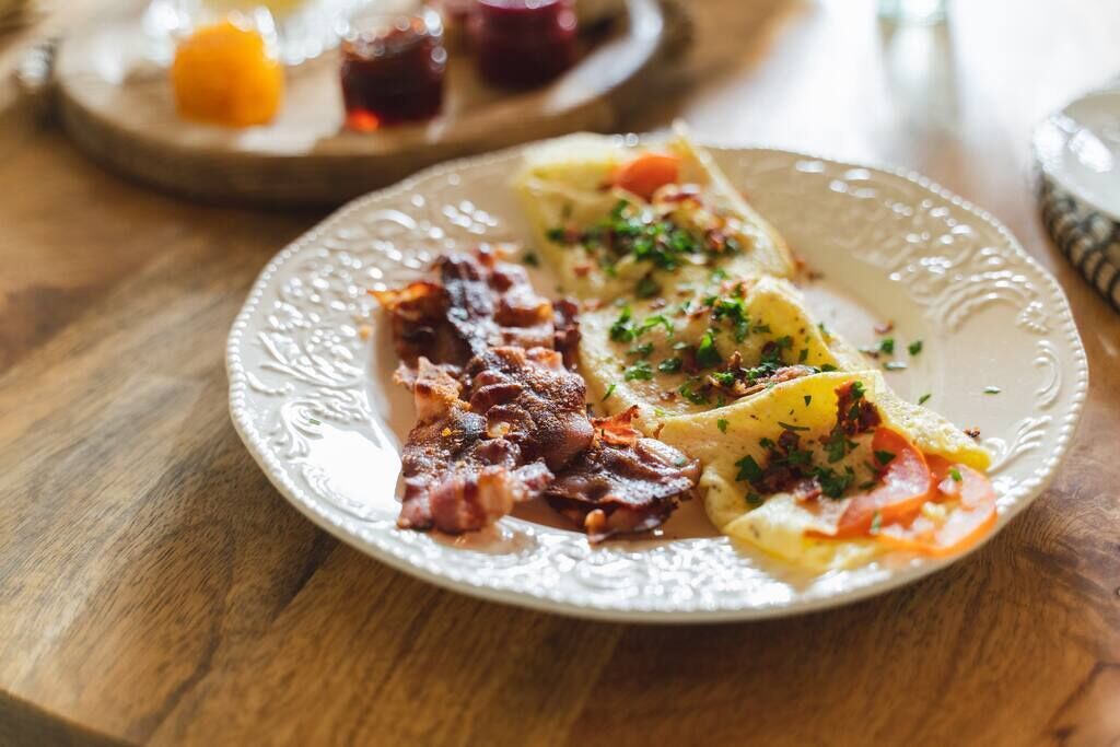A plate with bacon, scrambled eggs, and potatoes garnished with herbs.