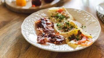 A plate with bacon, scrambled eggs, and potatoes garnished with herbs.
