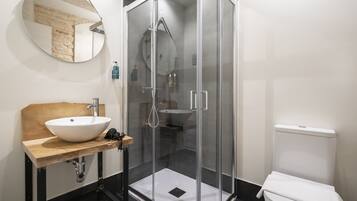 Un baño moderno con tocador de madera, ducha con cerramiento de vidrio y un inodoro blanco.