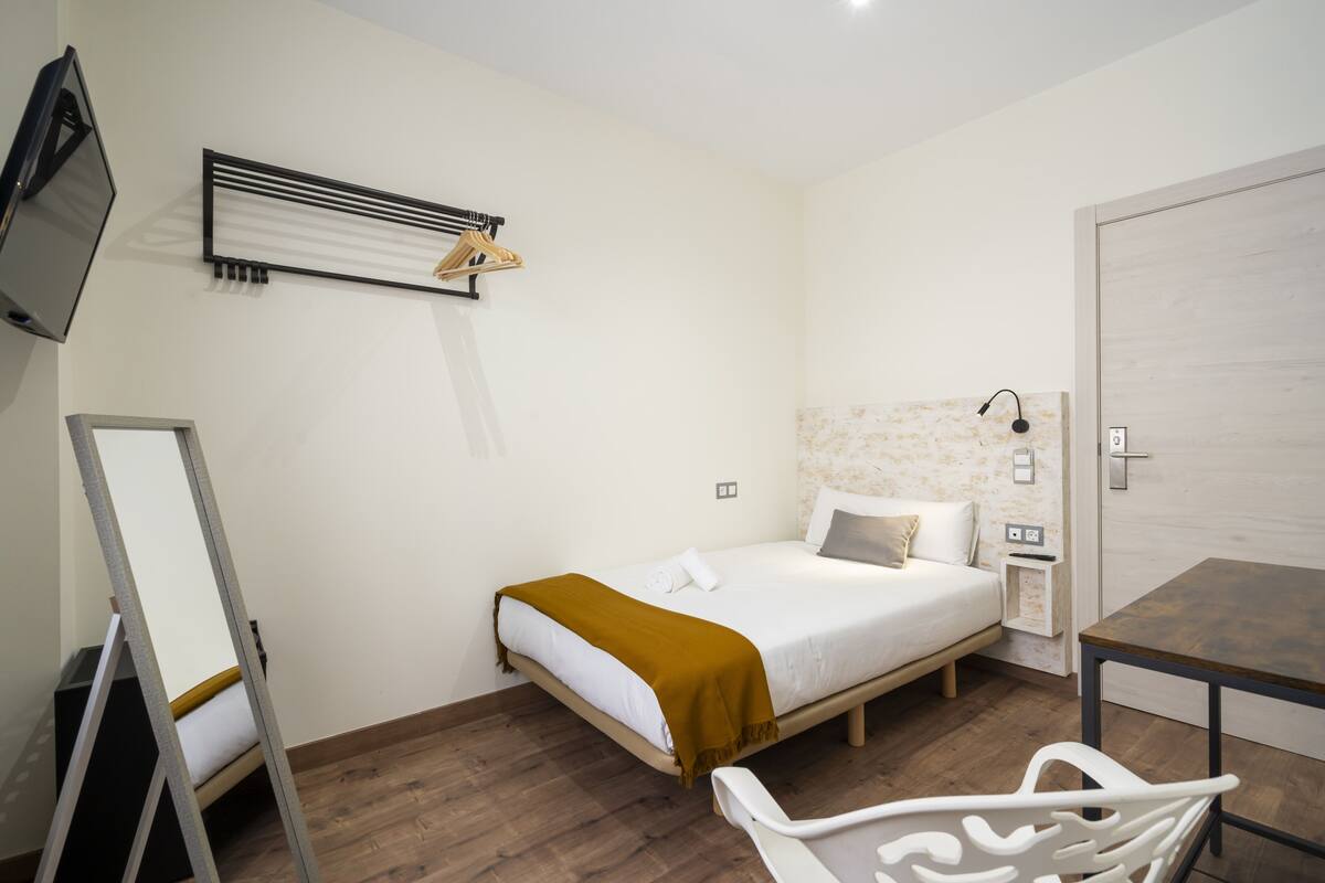 Un dormitorio con cama, mesita de noche y televisor instalado en la pared.