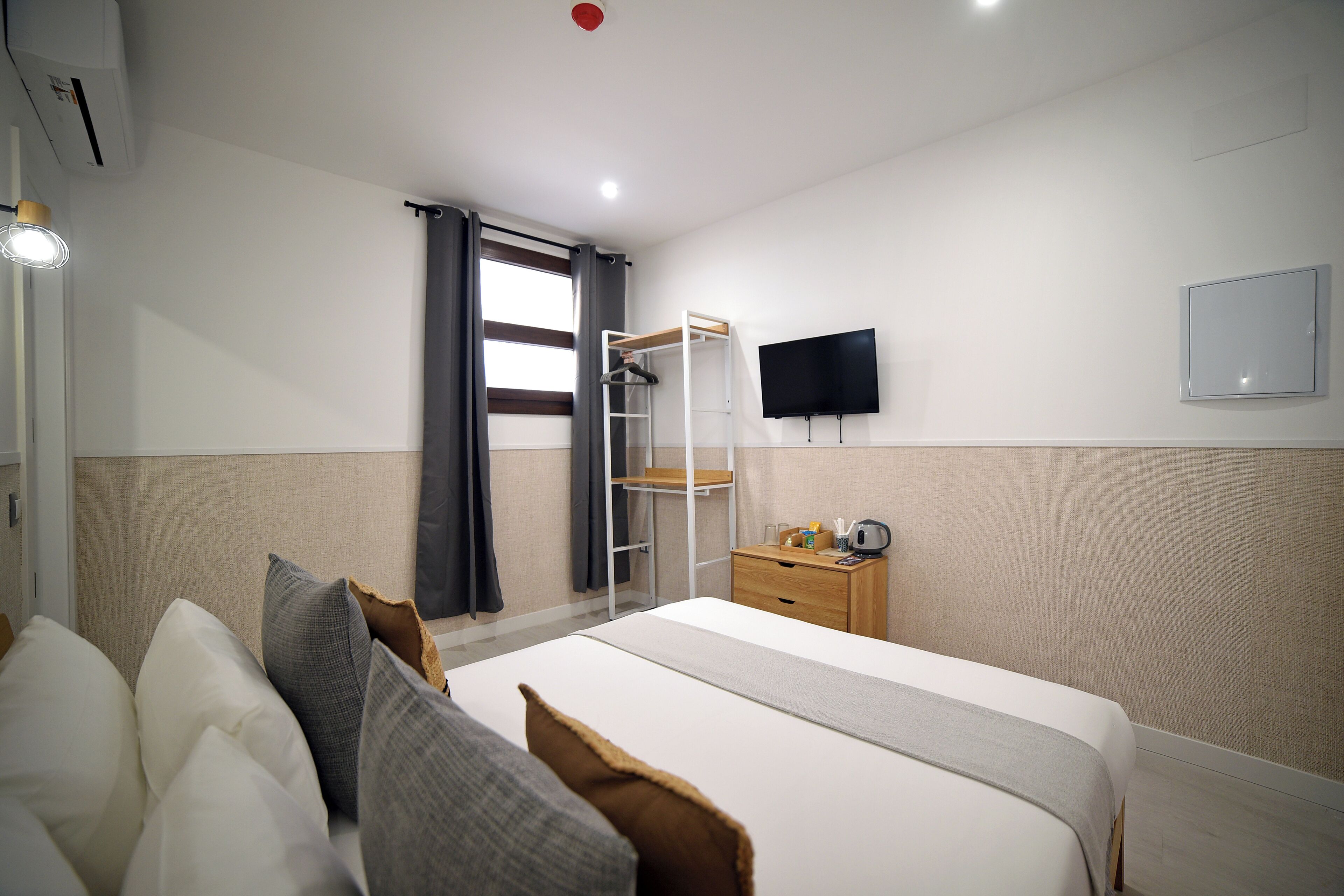 A hotel room with a bed, a wardrobe, a desk, a television, and a window with curtains.