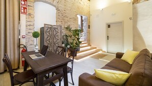 Un espacio de sala acogedor con pared de piedra, techo de madera, sofá marrón con cojines amarillos, mesa de comedor con sillas y una computadora portátil.