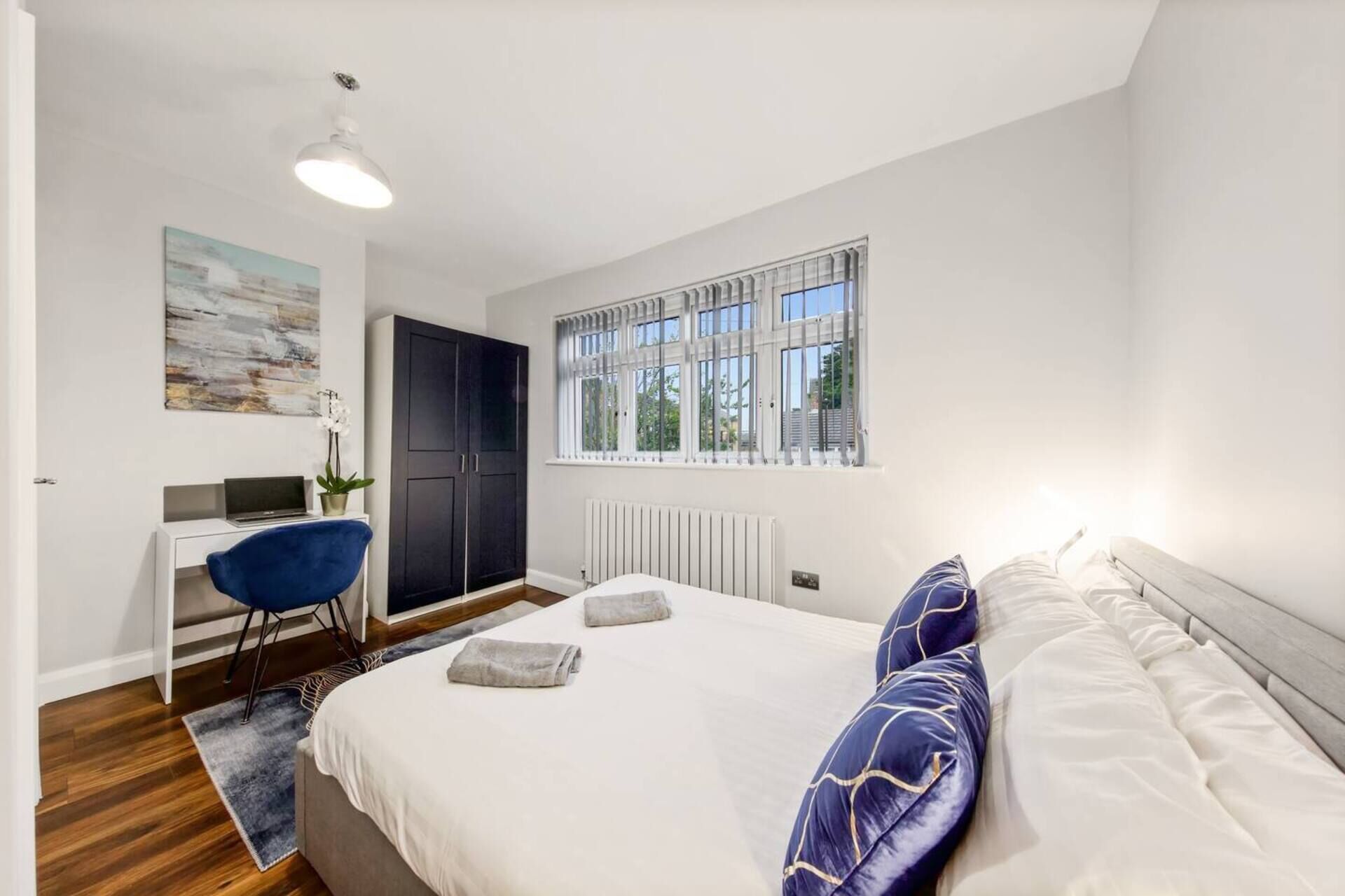 A bedroom with a bed, a desk, a chair, a radiator, and a window with blinds.