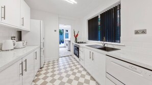 Una cocina moderna con armarios blancos, piso a cuadros y una ventana con persianas.