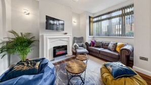 Una sala de estar con chimenea, un sofá, una mesa de centro y un televisor montado en la pared.
