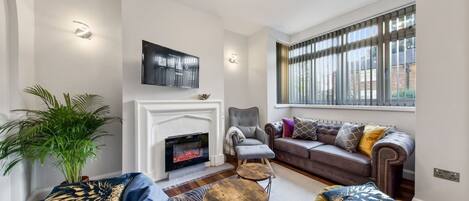 A living room with a fireplace, a sofa, a coffee table, and a TV mounted on the wall.