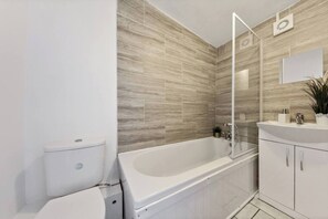 A modern bathroom with a freestanding bathtub, a toilet, and a vanity with a mirror. - Home Away From Home With an Indoor Fireplace! (London)