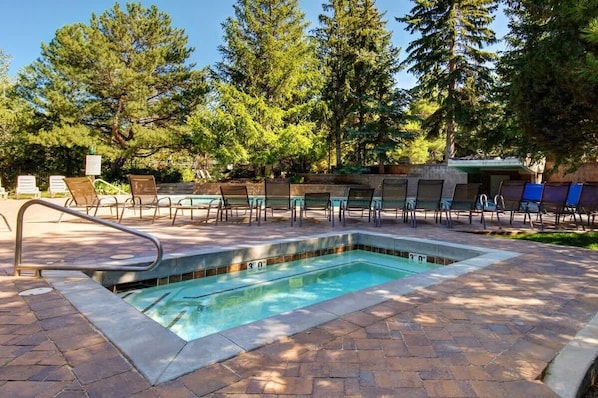 Una piscina rectangular con una escalera metálica, rodeada de sillas de descanso y un patio de ladrillo.
