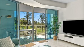 A modern living room with a sliding glass door leading to a balcony, a flat-screen TV, and a dining area with outdoor furniture.