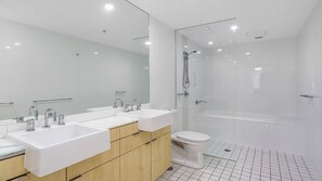 A modern bathroom with a double sink vanity, a toilet, and a glass-enclosed shower area.