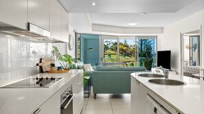 A modern kitchen with a built-in oven, a dining area with a green sofa, and a large window offering a view of the outdoors.