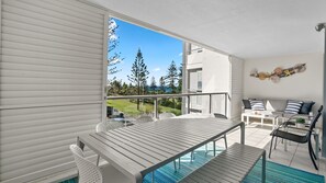 Een balkon met uitzicht op zee, een zithoek met een tafel en stoelen, en een decoratieve wand met schelpen en zeesterren.