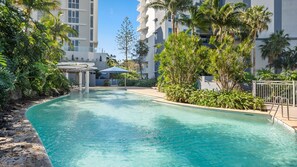 A swimming pool with a clear blue water, surrounded by lush greenery and modern buildings.