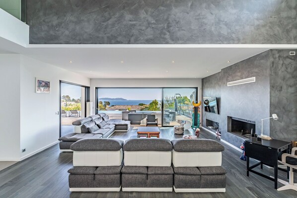 Un salon moderne avec un grand canapé d’angle gris, un téléviseur à écran plat fixé au mur et une cheminée.