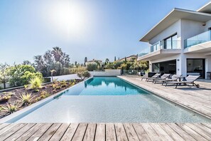 Un espace piscine moderne avec une terrasse en bois, des chaises longues et une piscine à l’eau d’un bleu cristallin.