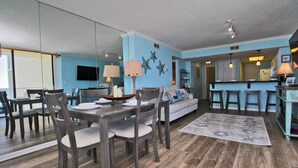 A modern living room with a dining area, a kitchen, and a bar area. - Condo in Gulf Shores | Beachfront Views from Private Corner Balcony | Sleeps 8 (Gulf Shores)
