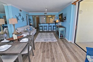 Un espace de vie compact comprenant un coin cuisine, une table à manger avec des chaises, un canapé et un comptoir-bar avec des tabourets.
