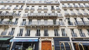 Un immeuble à plusieurs étages doté de balcons, d’une porte d’entrée centrale en bois et de boutiques, dont un restaurant.