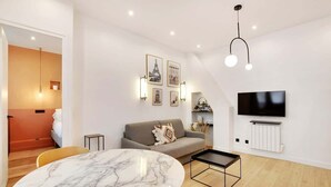 Un salon moderne avec une table en marbre, un canapé gris et un téléviseur à écran plat fixé au mur.
