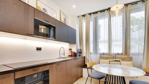 Une cuisine moderne dotée d’appareils électroménagers intégrés, un coin repas avec une table ronde et des chaises, et un espace détente avec un canapé et des rideaux.