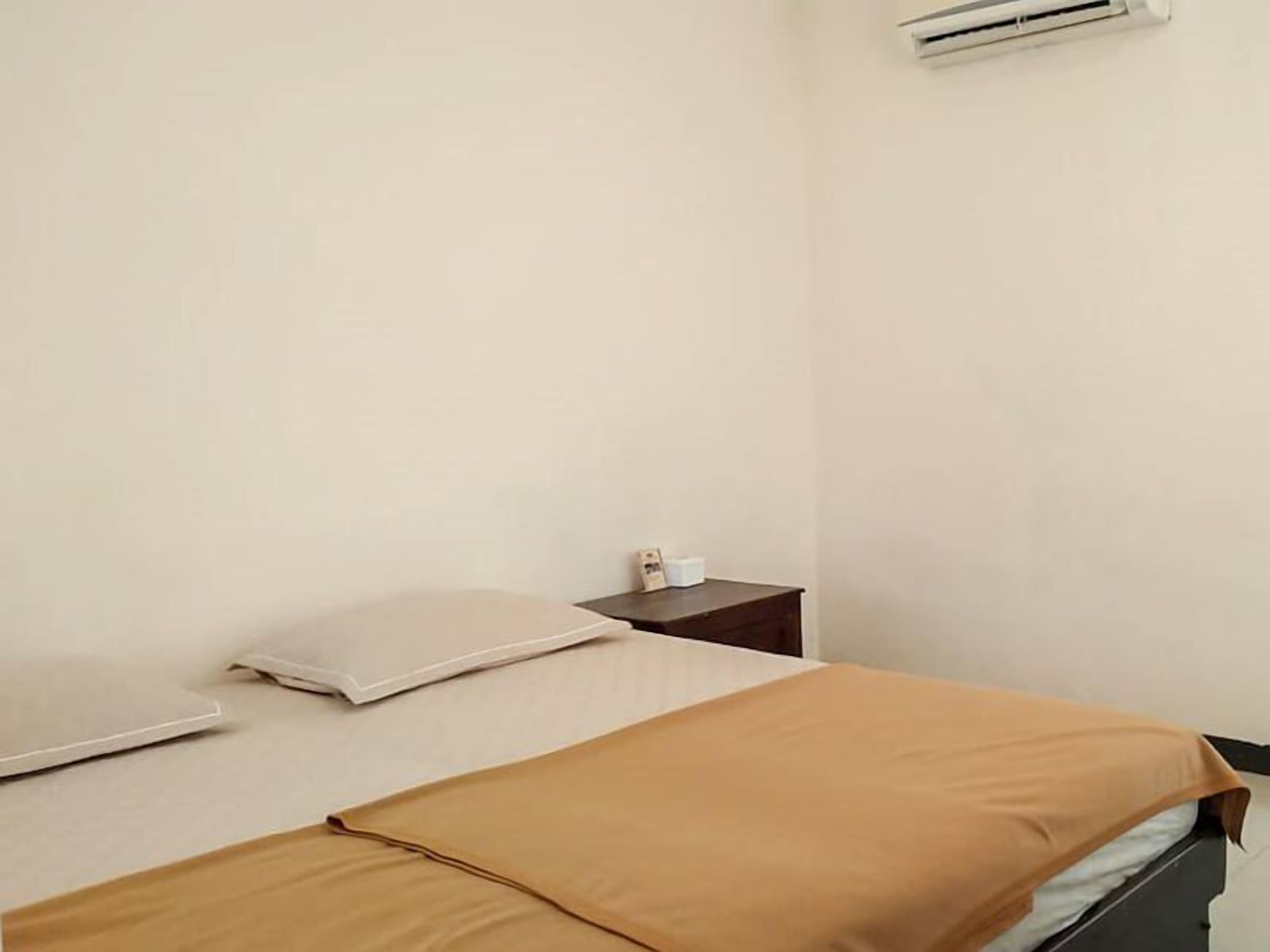 Una cama individual con una colcha marrón, una almohada blanca y una mesita de noche con lámpara.