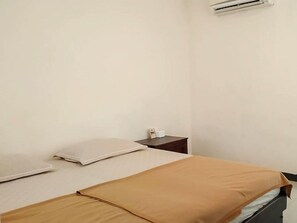 Un letto singolo con copriletto marrone, un cuscino bianco e un comodino con una lampada.