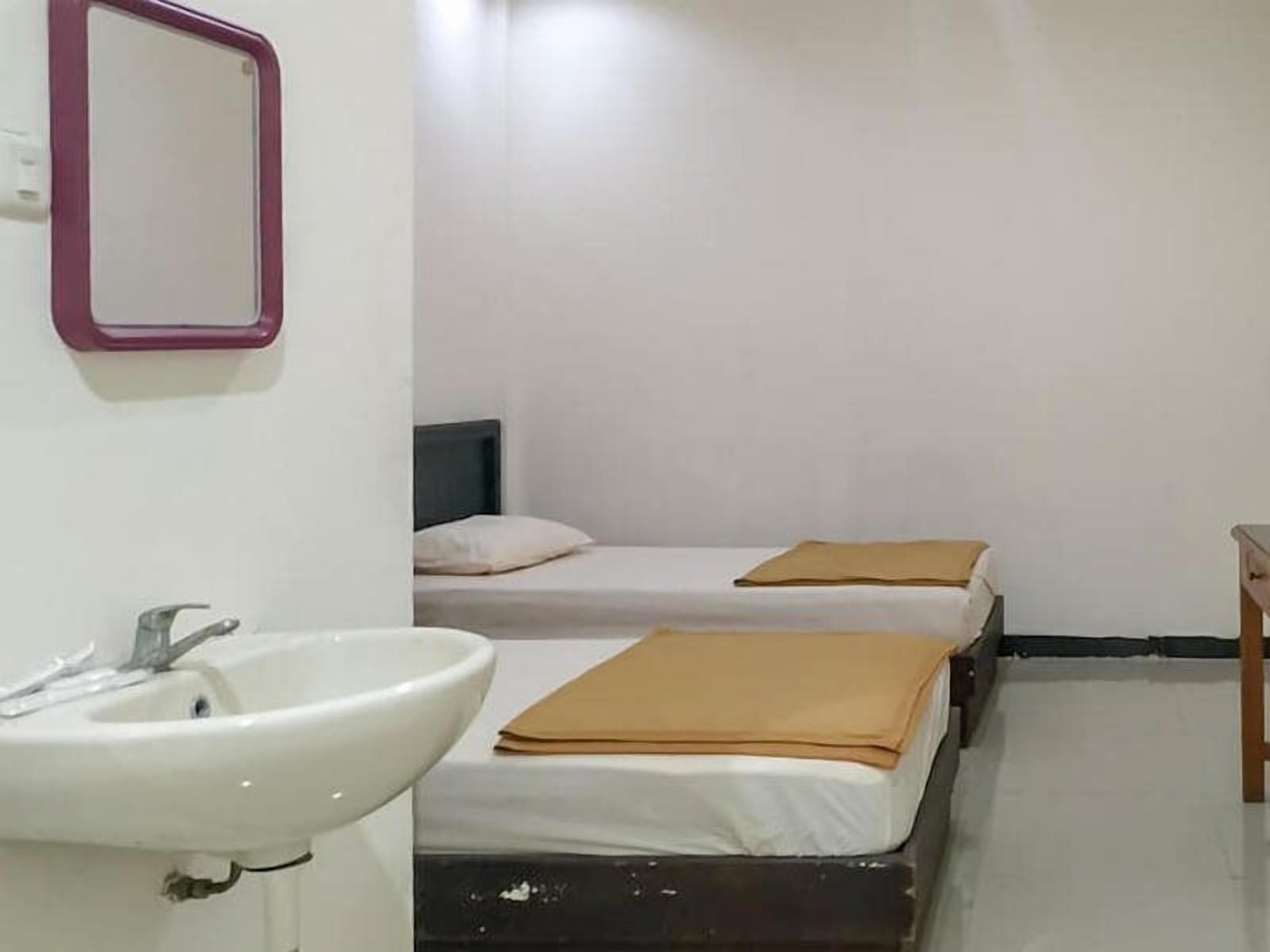 Una habitación con un lavamanos, dos camas con mantas marrones y una pequeña mesa de madera.