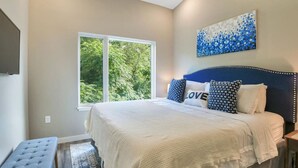 A bedroom with a large bed, a window with a view of trees, and a blue abstract painting on the wall.