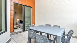 A modern outdoor dining area with a grey table and chairs, a sliding glass door leading to an interior space, and a tiled floor.