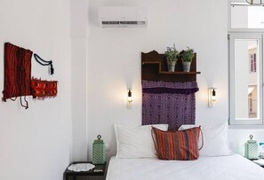 Quarto com cama, mesa de cabeceira, prateleira fixada na parede com plantas e ar-condicionado de parede.