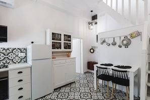 Cozinha compacta com armários brancos, painel de fundo padronizado e área de refeições com mesa e cadeiras.