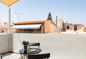 A rooftop terrace with a table and chairs, a potted plant, and a building with a red roof in the background. - The Residence of the Old Port (Rethymno)