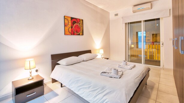 Habitación de hotel con cama, lámparas de noche, un cuadro, una puerta corrediza de vidrio y un equipo de aire acondicionado.