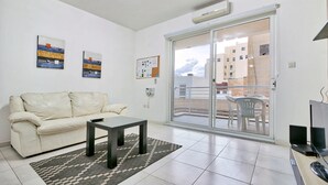 Una sala de estar con un sofá, una mesa de centro y un televisor. Hay dos cuadros en la pared y un tablón de anuncios.