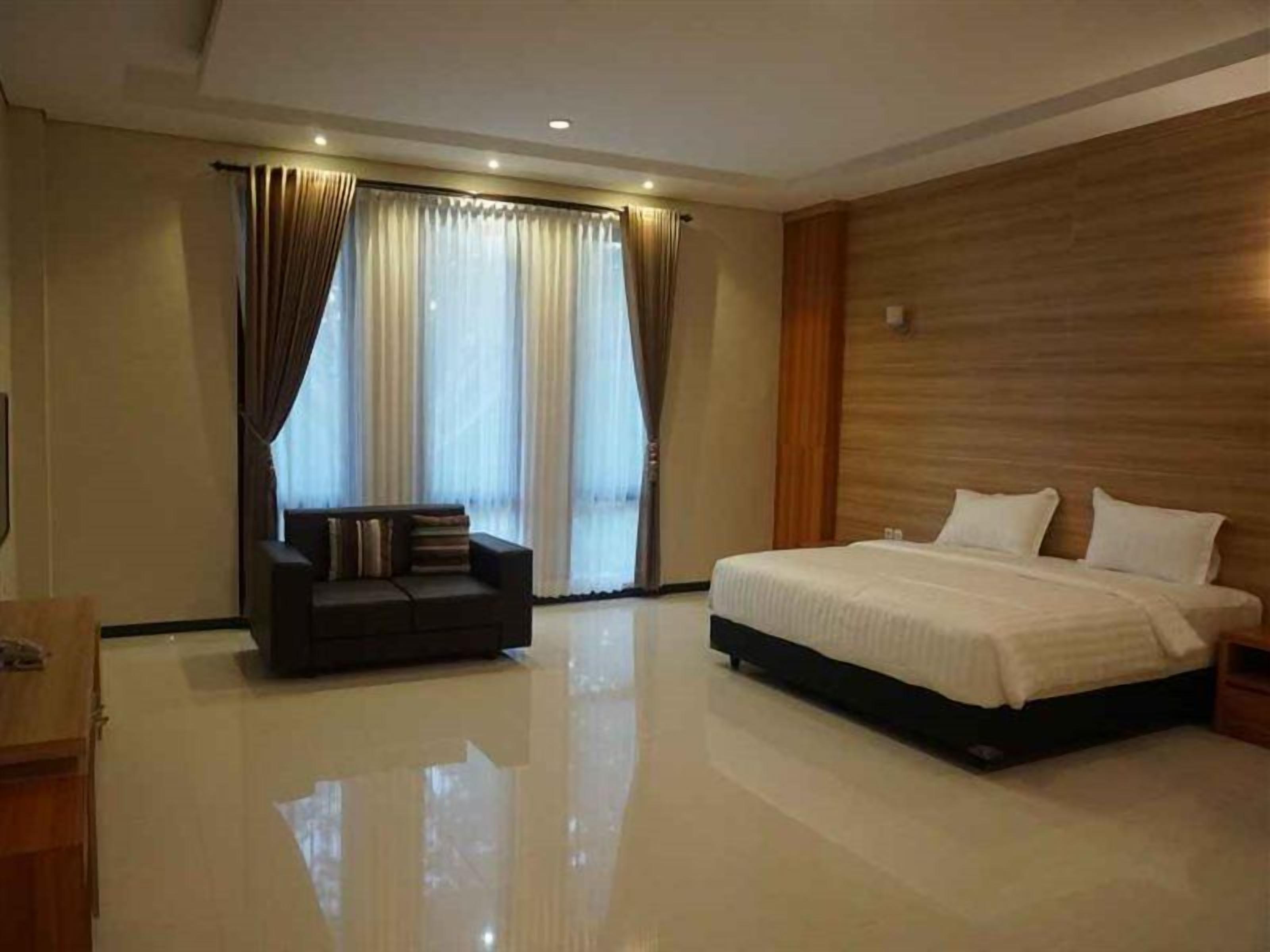 A modern hotel room with a large bed, a sofa, and a wooden accent wall.