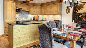A kitchen with wooden cabinets, a central island, and a dining area with a table set for four. - Bastide 014, Optimal sun exposure, quiet, central location (Verbier)