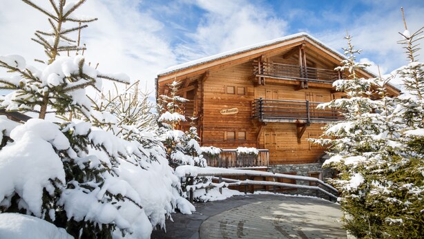 A wooden chalet with a balcony, surrounded by snow-covered trees. - Bastide 014, Optimal sun exposure, quiet, central location (Verbier)